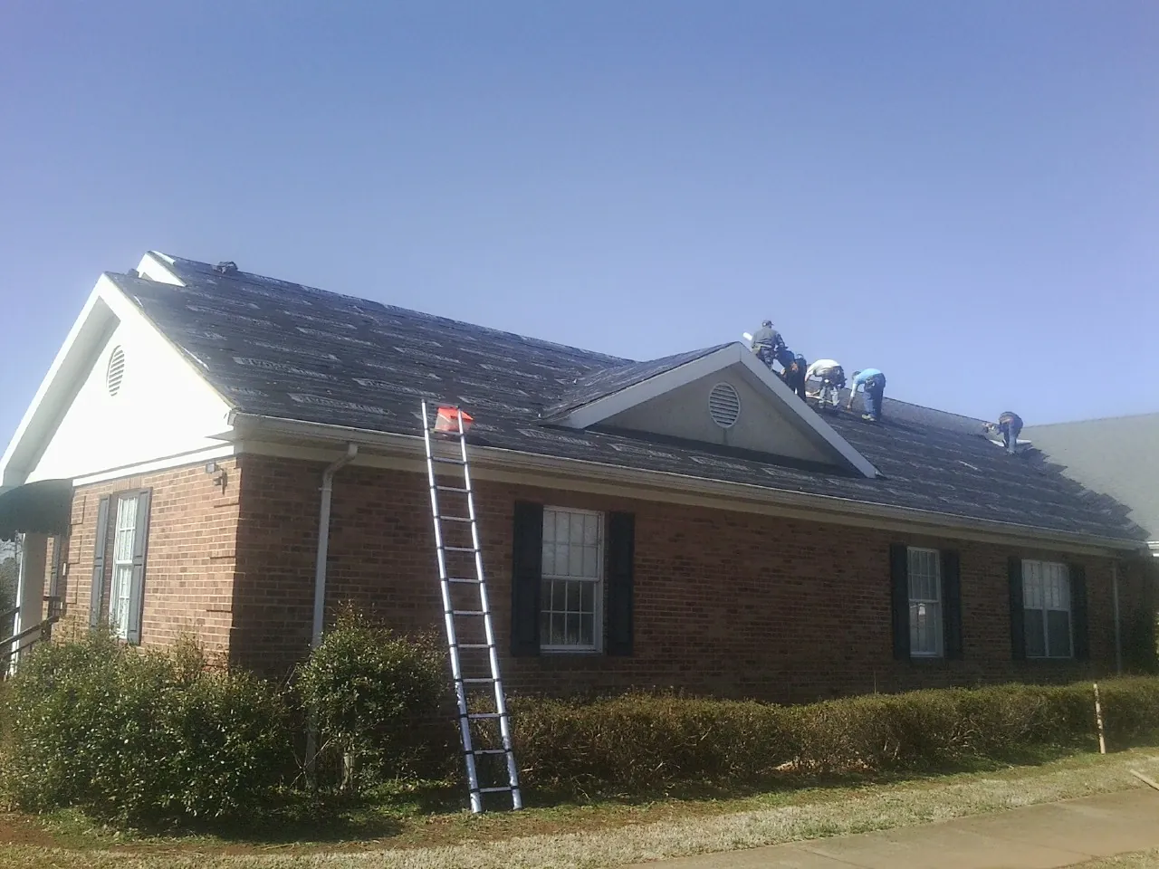 Crew tearing shingles off a brick ranch roof with a ladder set — Emergency Roof Repair work by our crew in Antrim