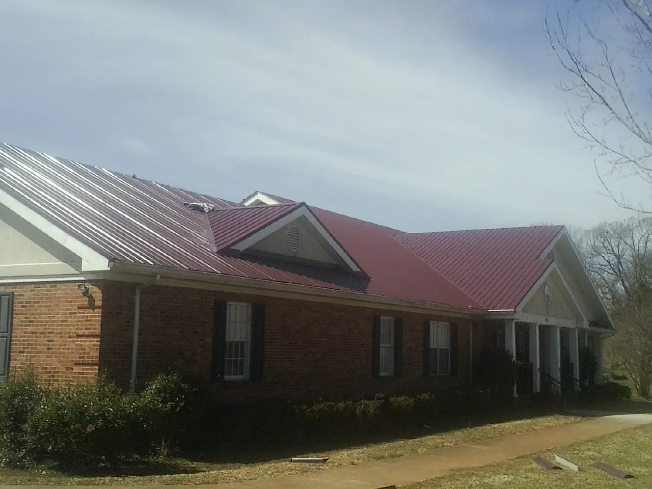 Red metal roof with gabled entries on a long brick building, from a Hail Damage Roof Repair job in Antrim