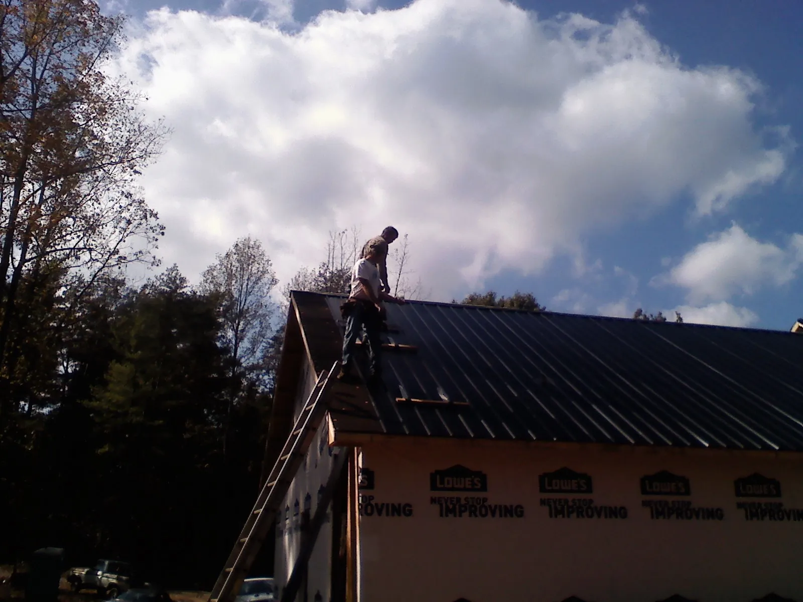 Roofer fastening dark metal panels high against a cloudy sky, from a Roof Inspection job in Antrim