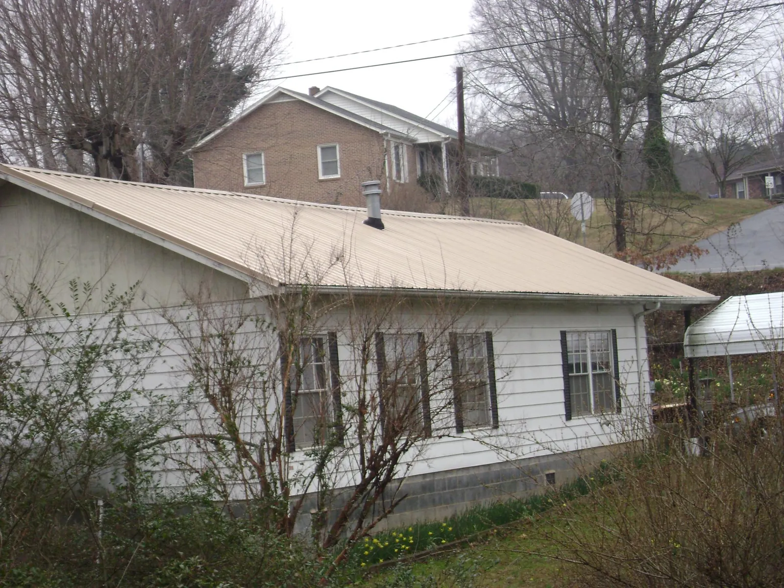 Tan metal roof on a white sided house set into a hillside — Commercial Roofing by Roofing Brothers in Antrim
