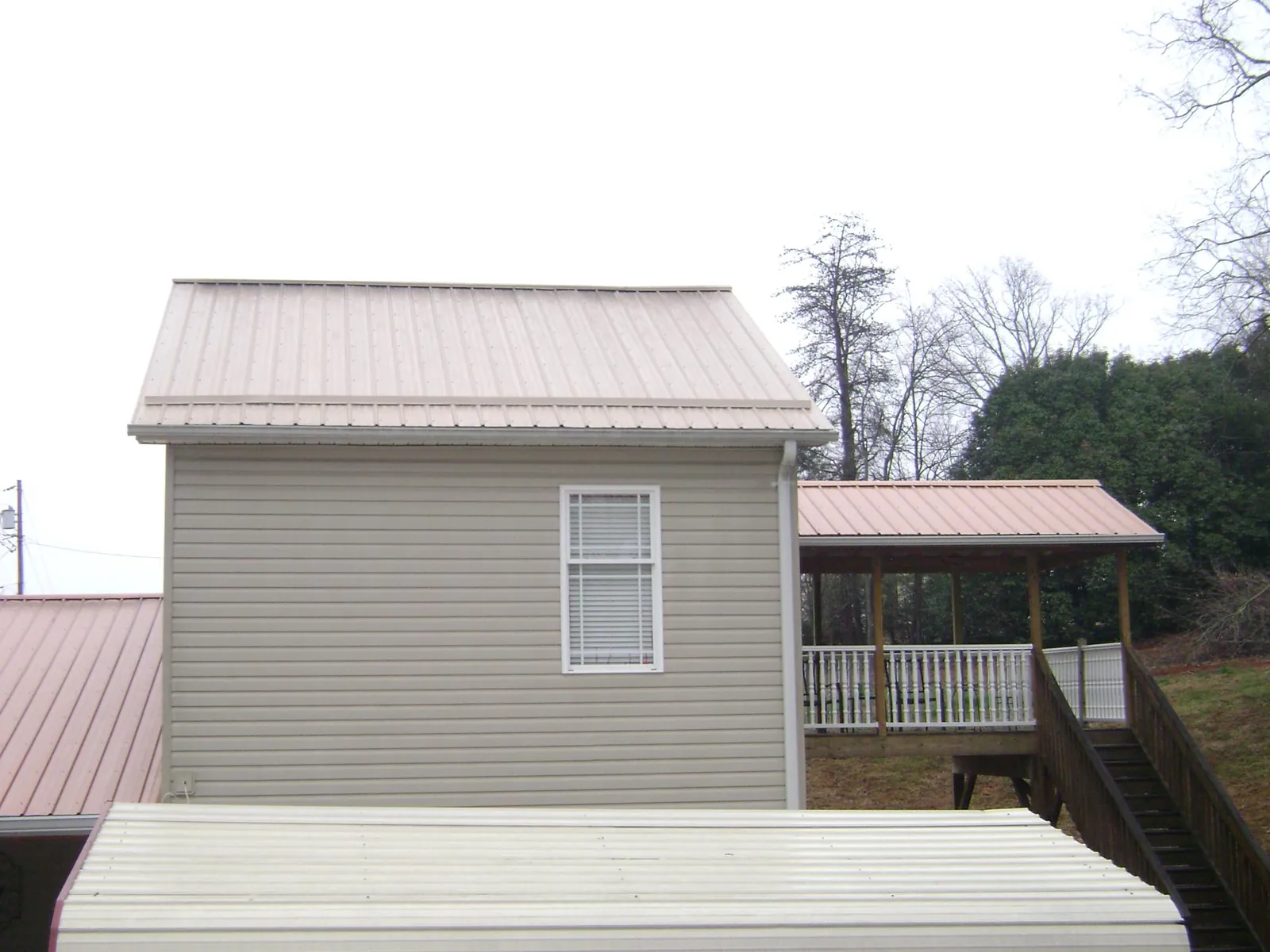 Tan metal roofs on a two story addition and attached porch, from a Roof Replacement job in Antrim